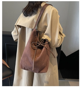 Detail of dark brown suede bucket bag with decorative leather bow and shoulder strap