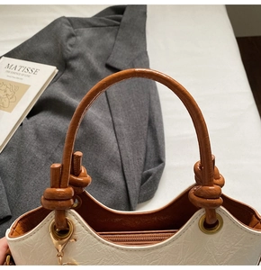 Detail of white textured bucket bag with brown ring handle and gold zipper hardware