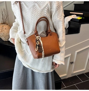Close-up of caramel leather bucket bag with chunky chain and chocolate pendant detail