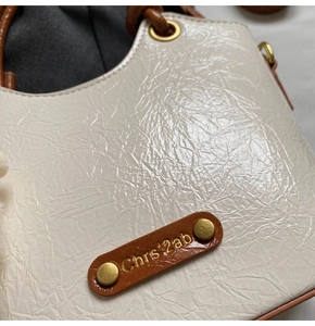 Detail of creamy white bucket bag featuring wrinkled patent leather and golden hardware