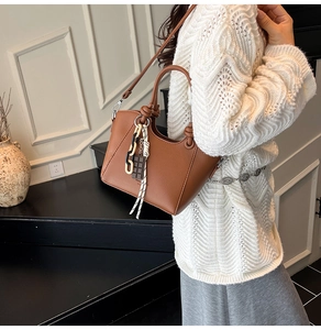 Detailed side view of a brown bucket bag with chocolate charm and chain detail