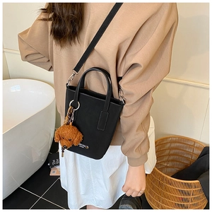 Détail du sac seau en cuir noir avec breloque caniche marron et finitions argentées