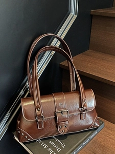 Retro brown underarm bag with large buckle and silver rivets on a wooden staircase