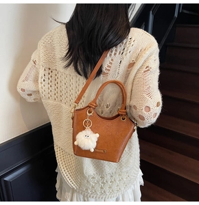 Close-up of brown textured leather bucket bag featuring a cute white lamb plush pendant