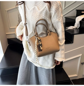 Detail view of khaki pebbled leather bucket bag with decorative chain and chocolate charm