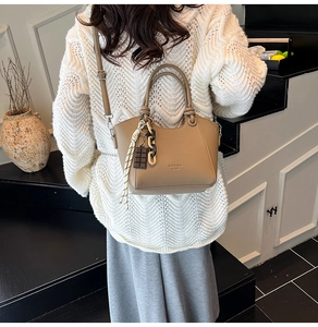 Macro detail of khaki litchi leather handbag with decorative charms and striped scarf