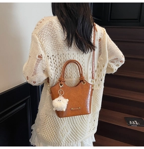 Detail of caramel leather bucket bag featuring a plush sheep pendant on wooden stairs