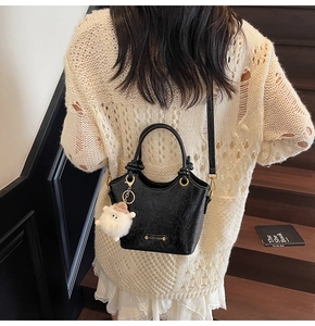 Close-up of black pleated patent leather bucket bag with gold logo and plush lamb charm