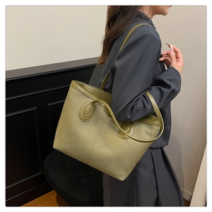 Detail of olive green canvas tote bag with leather trim worn by a model in a minimalist setting