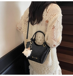 Detail of black glossy bucket bag with metal ring handles and a cute plush sheep charm