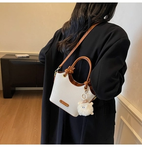 Detailed close-up of white pleated bucket bag with brown leather handles and plush charm