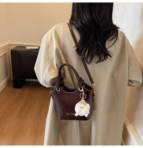 Detail of dark brown wrinkled leather bucket bag with cream plush charm and gold hardware
