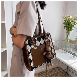 Detailed side view of a large brown argyle tote bag with a cute rabbit doll charm