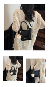 Detail of black textured bucket bag with a plush sheep charm and crossbody strap