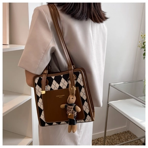 Detailed view of argyle tote bag with brown leather accents and a plush rabbit charm