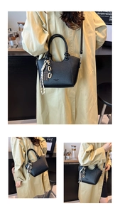 Detail of black pebbled leather bucket bag with gold chain and chocolate charm