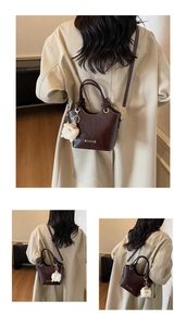 Detailed view of dark brown glossy bucket bag with plush charm and gold hardware