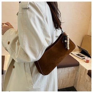 Détail d'un sac à bandoulière marron mat avec pompon en perles sur un manteau beige