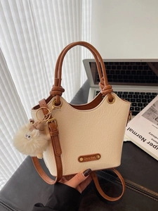 Beige pleated bucket bag with brown handles and white pom-pom charm in a modern office setup