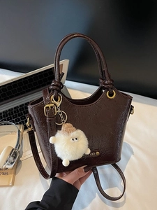 Deep brown textured leather bucket bag with plush charm on a cozy workspace desk