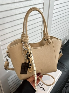 Beige litchi grain tote bag with knotted handles and fashion charms on a sofa