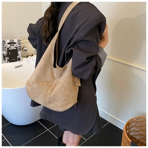 Close-up of a khaki suede hobo tote bag worn by a model in a warm interior setting
