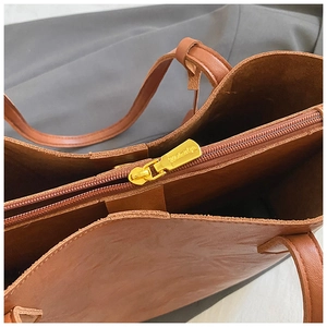 Gros plan du sac cabas en cuir marron montrant le grain et la fermeture éclair dorée