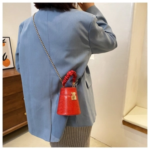 Dettaglio mini borsa rossa coccodrillo con catena dorata e manico arricciato su una modella