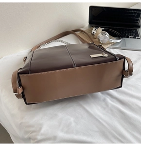 Détail de couture contrastée et chaîne en métal sur un sac cabas en similicuir marron