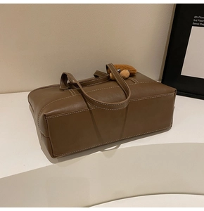 Détail du sac cabas marron montrant les surpiqûres et un joli pendentif d'ours
