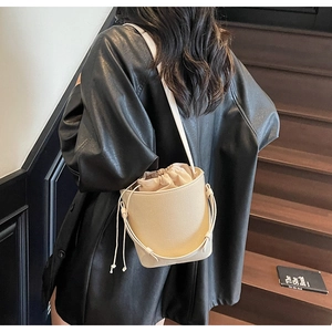 Primer plano del bolso saco beige texturizado con cierre de cordón y correa delgada