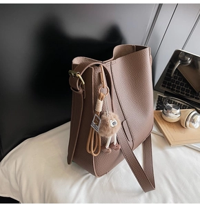 Detail of brown litchi pattern leather bucket bag with plush charm on office desk