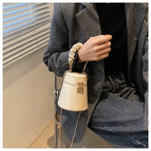 Dettaglio borsa a cilindro beige coccodrillo con manico arricciato e catena dorata