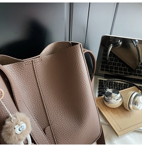 Detail of taupe pebbled leather shoulder bag with cute plush cat charm and soft lining