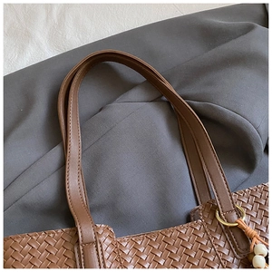 Detail of dark brown woven tote bag showing leather texture and wooden bead charm