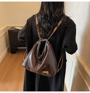 Détail d'un sac cabas marron foncé brillant avec poignées chaînes porté par modèle