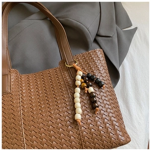 Detail of brown woven leather tote bag with colorful decorative beaded charm