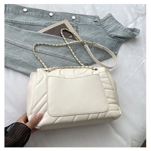 Detail of white quilted chain bag with V-shaped stitching on soft denim fabric