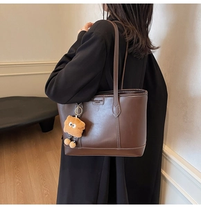 Détail d'un sac cabas en cuir marron foncé avec un charm ours en peluche et étiquette