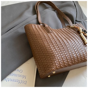 Detailed weave pattern on brown tote bag with beaded tassel and gold bottom studs