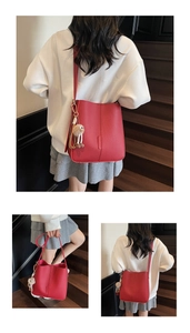Detailed view of red textured bucket bag with plush charm on indoor wooden stairs