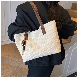 Detail of white woven tote bag with brown straps and beaded charm worn by a model