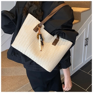Close-up of off-white woven tote bag with brown handles and bead tassel on a female model