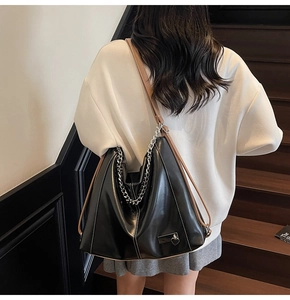 Détail du sac hobo noir avec chaîne argentée et bandoulière marron porté par un modèle