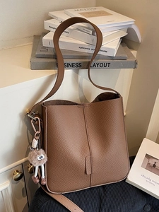 Brown litchi leather bucket bag with shoulder strap and pink plush charm in a minimalist setting