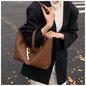 Detail of a brown hand-woven leather tote bag with classic crisscross texture and beads