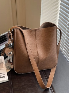 Brown litchi leather bucket bag with wide strap and plush eye charm in warm sunlight