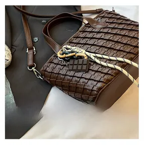 Close-up of brown woven leather tote with chocolate charm and crossbody strap details