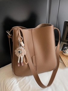 Caramel brown pebbled leather bucket bag with wide strap and plush pendant in lifestyle setting