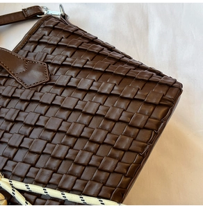 Detail of dark brown woven faux leather bucket bag with decorative textured rope strap